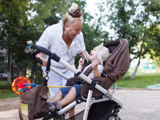 Granny playing with her grandson in a baby stroller in the yard.